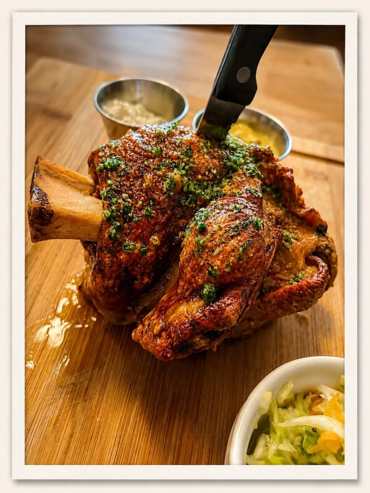 Photo of roasted pork knuckle from Na Hradčanské in Prague, served on a wooden board with sauces and a small bowl of cabbage salad.